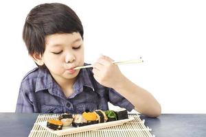 menino adorável asiático está comendo sushi sobre fundo branco foto