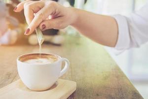 closeup de senhora derramando açúcar enquanto prepara a xícara de café quente foto