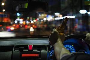 homem bebe cerveja enquanto dirige à noite na cidade perigosamente, sistema de volante à esquerda foto