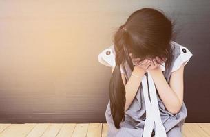 menina asiática triste sentada no chão de madeira branca foto