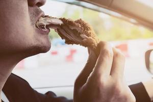 homem de negócios dirigindo carro enquanto come frango frito perigosamente foto