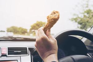 homem de negócios dirigindo carro enquanto come frango frito perigosamente foto