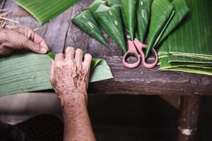 mãos de avó velha trabalhando com folha de bananeira para fazer recipiente de flores - pessoas fazendo item tradicional para participação em cerimônia local foto