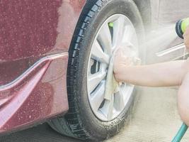 a mão de um homem está limpando uma roda de carro usando pano e spray de água foto
