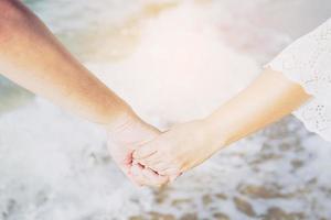 casal asiático está de mãos dadas perto do mar com céu de luz do sol quente foto