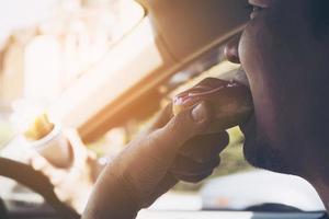 homem comendo donuts e batata frita enquanto dirige o carro - conceito de condução insegura multitarefa foto