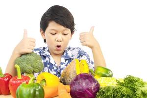 menino saudável asiático mostrando expressão feliz com variedade de vegetais coloridos frescos sobre fundo branco foto