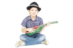 menino asiático de 7 anos está sentado e tocando ukulele isolado sobre o branco. foto