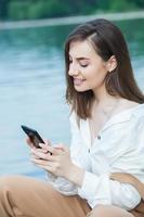 garota ao ar livre mensagens de texto em seu celular. menina com telefone. retrato de uma mensagem de sms de texto de mulher feliz em seu telefone. foto
