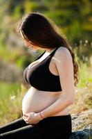 mulher grávida com cabelo longo e saudável e flores. linda garota esperando o bebê. futura mãe abraça sua barriga. foto