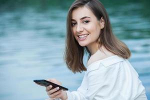 garota ao ar livre mensagens de texto em seu celular. menina com telefone. retrato de uma mensagem de sms de texto de mulher feliz em seu telefone. foto