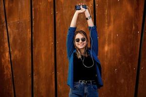 foto de uma jovem estudante bonita sorridente alegre usando óculos escuros ao ar livre usando telefone celular conversando ouvindo música com fones de ouvido.