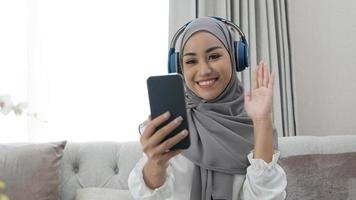 mulher muçulmana asiática milenar atraente tendo uma chamada de vídeo de seus amigos na sala de estar. foto
