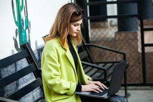 a garota trabalha no computador em um café. aluno aprendendo on-line. blogueiro. jovem escritora caucasiana digitando no laptop. mulher de negócios atraente usando computador portátil durante uma pausa. foto