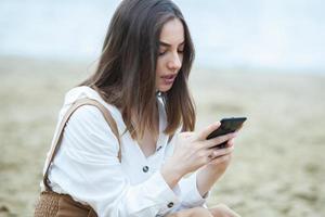 garota ao ar livre mensagens de texto em seu celular. menina com telefone. retrato de uma mensagem de sms de texto de mulher feliz em seu telefone. foto