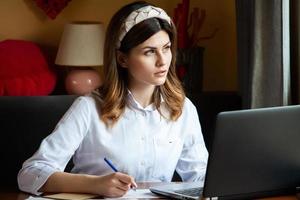 a garota trabalha no computador em um café. aluno aprendendo on-line. blogueiro. jovem escritora caucasiana digitando no laptop. mulher de negócios atraente usando computador portátil durante uma pausa. foto