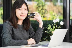 jovem mulher segurando cartão de crédito com computador portátil no convés foto