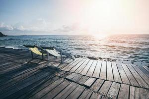vista do terraço das ondas do mar e paisagem costeira rock com cadeira de banco praia na ilha tropical da varanda da ponte de madeira com céu azul do oceano e fundo do resort na praia de verão da tailândia foto