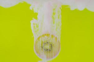 foco desfocado de dissolver a cor do pôster rosa na água com fatia de kiwi em fundo amarelo foto