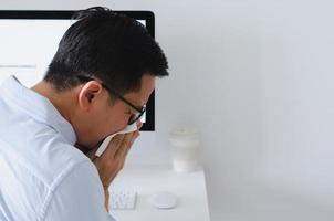 homem asiático espirrando em guardanapo no local de trabalho para o conceito de gripe e vírus. foto