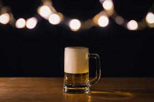 um copo de cerveja na mesa de madeira que tem luzes de bokeh em cima com fundo escuro. foto
