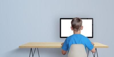 menino aprende a codificar no conceito de computador desktop. um menino de camisa azul com as costas viradas. copie o espaço de lado. exibição de computador isolada para promoção de página foto