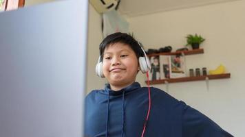 sorridente menino asiático segurando as mãos atrás da cabeça sentado atrás de usar o laptop do computador. estudante feliz se sentindo relaxante, depois de aprender educação on-line bem-sucedida em casa foto