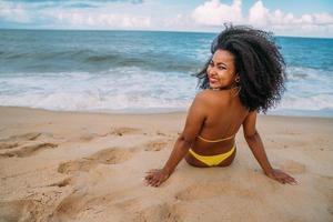 silhueta de jovem na praia. mulher latino-americana sentada na areia da praia olhando para a câmera em um lindo dia de verão foto