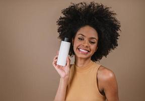 mulher latina de beleza com penteado afro. mulher brasileira. segurando a embalagem de xampu em branco. cabelo encaracolado. Penteado. fundo pastel. foto