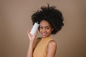 mulher latina de beleza com penteado afro. mulher brasileira. segurando a embalagem de xampu em branco. cabelo encaracolado. Penteado. fundo pastel. foto