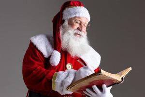 papai noel com um velho livro de capa vermelha. anotar nomes de presentes para o natal. o Natal está chegando foto