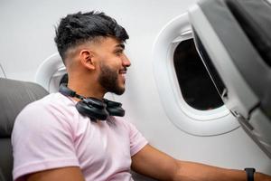 passageiro do avião, olhando para a janela sorrindo. homem latino-americano na cabine do avião, com fones de ouvido. foto