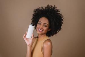 mulher latina de beleza com penteado afro. mulher brasileira. segurando a embalagem de xampu em branco. cabelo encaracolado. Penteado. fundo pastel. foto