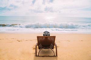 férias de verão, tecnologia e conceito de internet. homem latino-americano sentado na cadeira de praia, ouvir música com fone de ouvido e tomar sol na praia foto