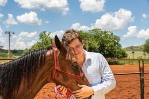 jovem criador de cavalos confortando um cavalo no rancho foto