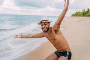 amigável confiante e sorridente jovem latino-americano com os braços abertos, olhando para a câmera na praia foto
