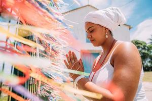mulher brasileira vestida com o traje tradicional baiano da religião umbandista fazendo uma oração. foco em fitas coloridas de promessas religiosas em devoção ao senhor do bonfim na bahia, brasil foto