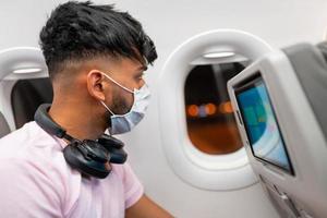 jovem latino-americano usando máscara facial protetora, viajando de avião. nova viagem normal após o conceito de pandemia covid-19 foto