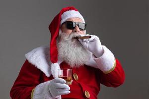 papai noel usando óculos escuros fumando um charuto e bebendo batedor em fundo escuro foto