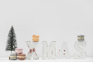 a palavra de madeira natal com biscoitos coloridos ou macarons e árvore de natal em fundo branco. decoração de natal. decoração de ano novo foto
