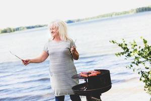 mulher sênior fazendo churrasco à beira do lago. foto
