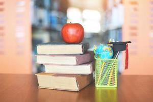 livros na mesa na biblioteca - educação aprendendo pilha de livros antigos e chapéu de formatura em uma caixa de lápis com modelo de globo terrestre na mesa de madeira e fundo de sala de estante turva com maçã no livro foto