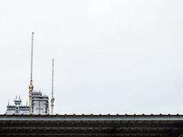 dois guindastes de construção estão trabalhando na construção de edifícios altos, levantando e colocando coisas. o canteiro de obras é coberto com cobertores. no edifício da cidade do céu branco em linha reta foto