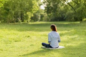 parte traseira da mulher asiática praticando meditação no parque. através da felicidade da paz interior. foto
