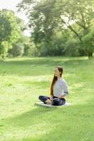meditação ao ar livre. mulher feliz fazendo meditação e relaxando no parque. meditação na natureza. conceito de estilo de vida saudável e relaxamento. mulher bonita praticando meditação na grama foto