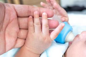 a mão esquerda do bebê está segurando a mão do pai enquanto bebe leite. foto