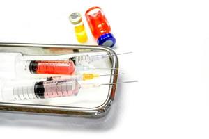 vacina em frascos e seringas de plástico com agulhas médicas colocadas em um recipiente médico de aço inoxidável para injeção pronta ao paciente em fundo branco. foto