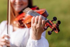 menina está tocando violino ao ar livre com jardim ao fundo em dia ensolarado de verão. imagem com foco seletivo e espaço de cópia. foto