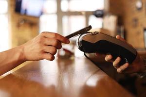 mão desconhecida macro dando terminal ao visitante para pagamento por telefone móvel interno. mão do cliente pagando conta com smartphone em fundo desfocado. mãos de tiro cortadas fazendo transações sem contato dentro. foto