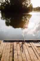 pesca do pôr do sol. pescador com vara de fiar. pescador com vara, molinete na margem do rio. pesca de lúcios, percas, carpas. natureza selvagem. artigo sobre o dia da pesca. foco seletivo na vara de pescar foto